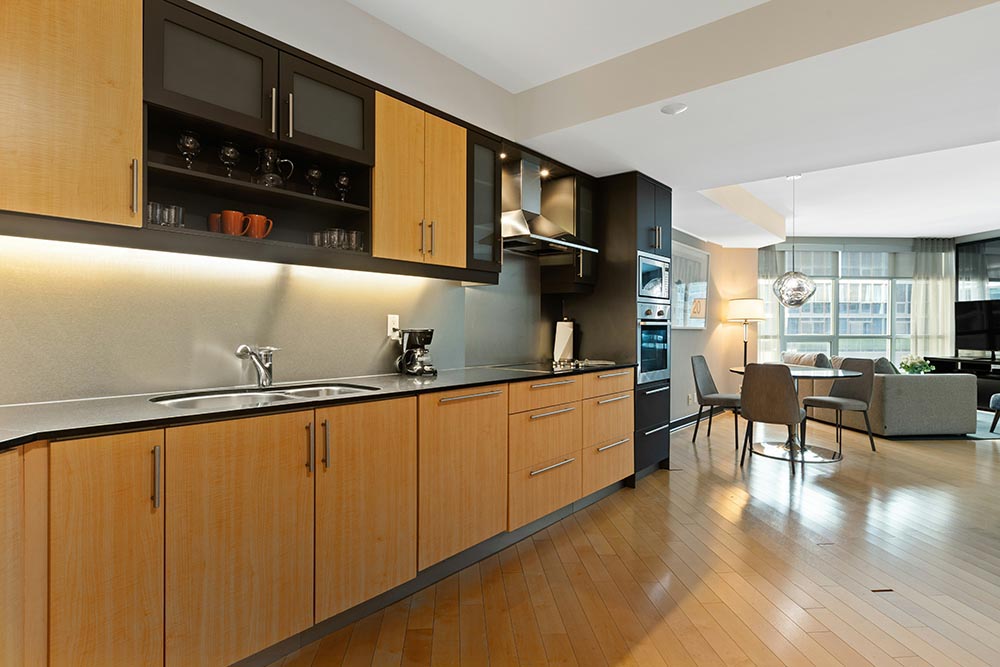 Kitchen remodel in Chicago with integrated light wood cabinets, black countertops, stainless steel appliances, and an open dining and living area with large windows.