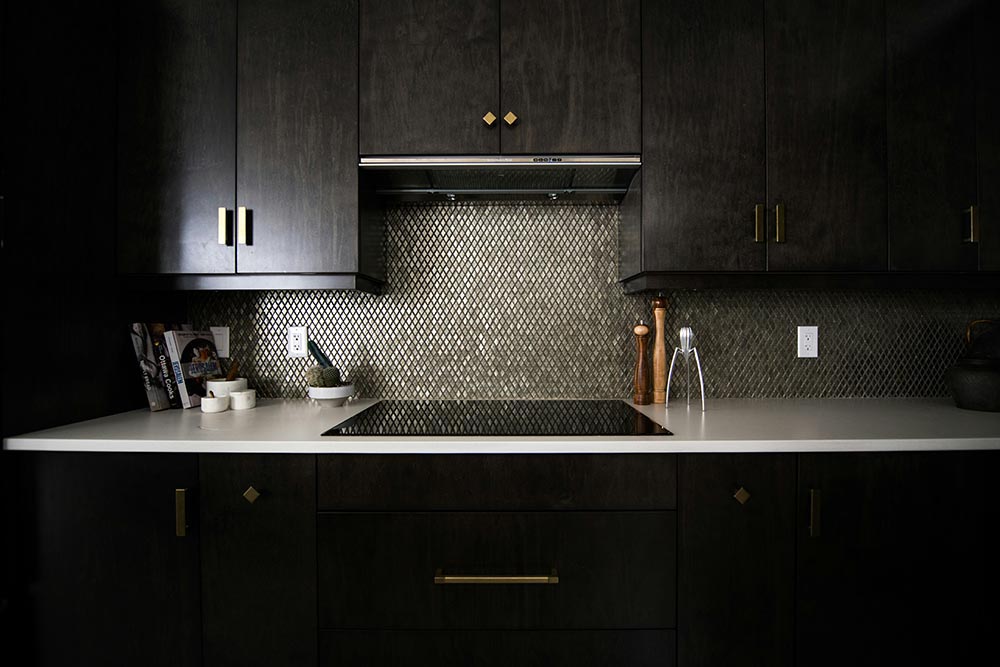Modern kitchen with dark wood cabinets, a white countertop, a geometric tile backsplash, and a black cooktop.