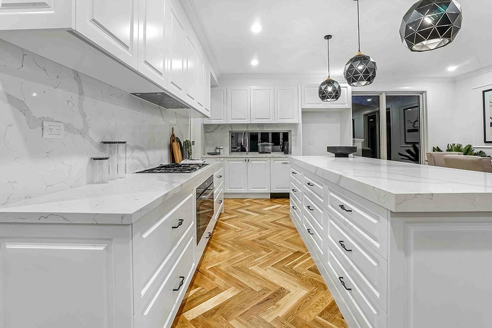 Modern white kitchen remodel in Chicago with marble countertops, geometric pendant lights, and herringbone wood flooring.
