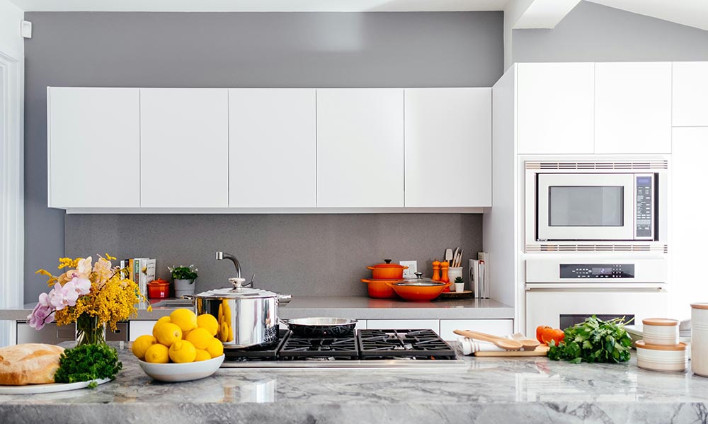Kitchen remodel in New York with white cabinets, stainless steel stove, a bowl of lemons, fresh herbs, and flowers on a marble countertop.