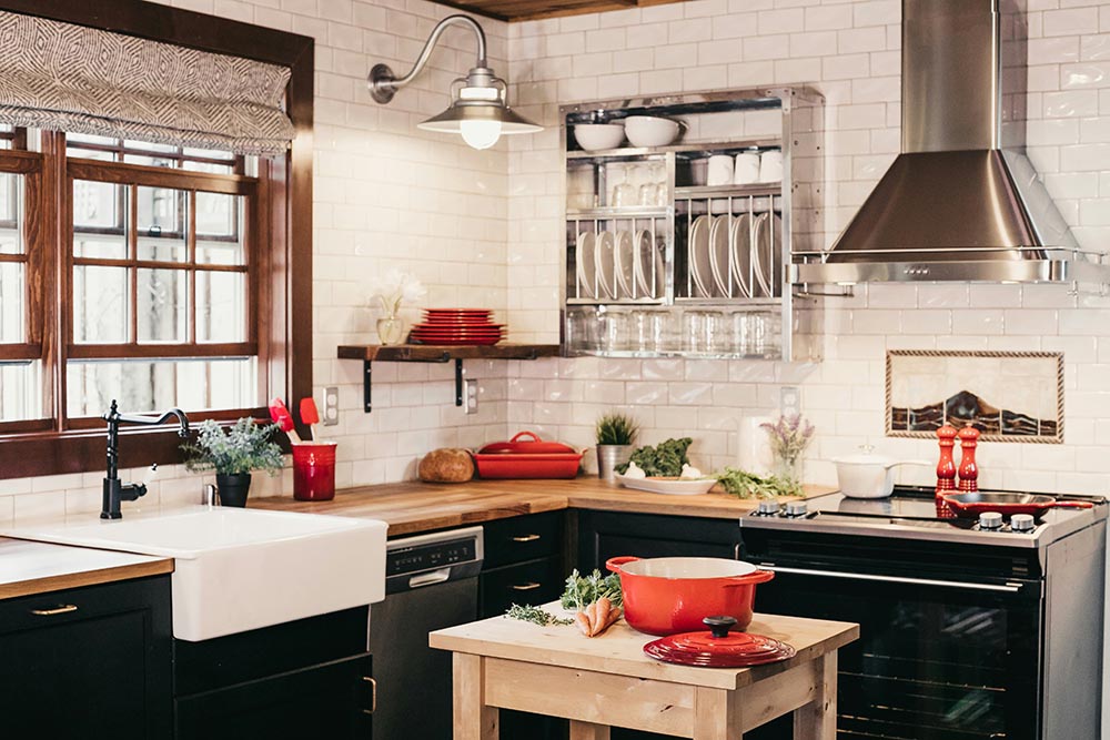 Cozy kitchen remodel in Chicago with wooden countertops, white farmhouse sink, red cookware, black cabinets, and a stainless steel range hood over a stove.