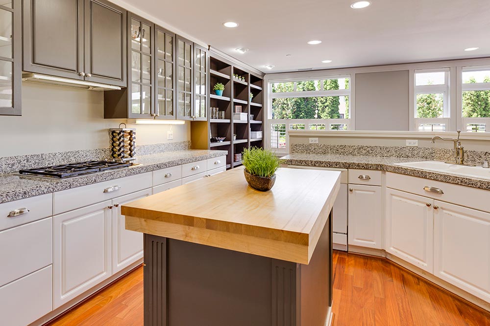 Kitchen remodel in New York with white cabinets, granite countertops, center island with wooden top, and large windows overlooking greenery.