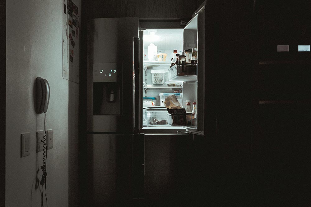 Dimly lit kitchen with a stainless steel refrigerator door open, showing various food items inside.