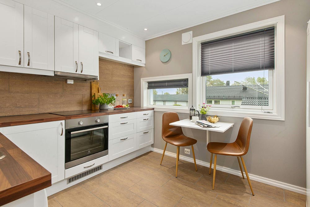 Kitchen remodel in Houston with white cabinets, wooden countertops, built-in oven, small dining table with two brown chairs near windows with blinds.