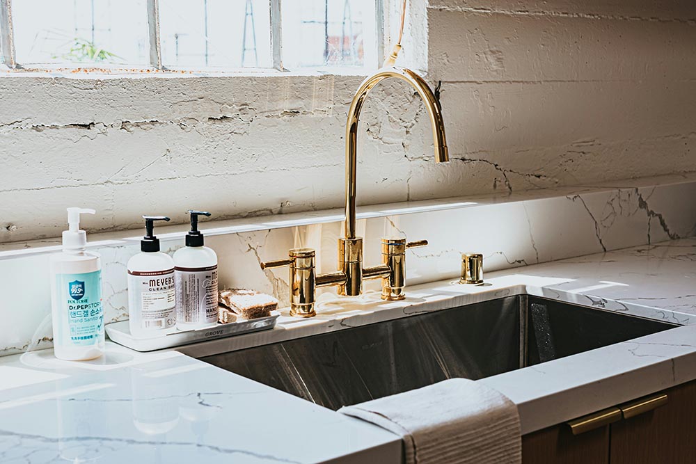 Kitchen remodel in Los Angeles sink with gold faucet, white marble countertop, hand soap bottles, and a towel draped over the edge.