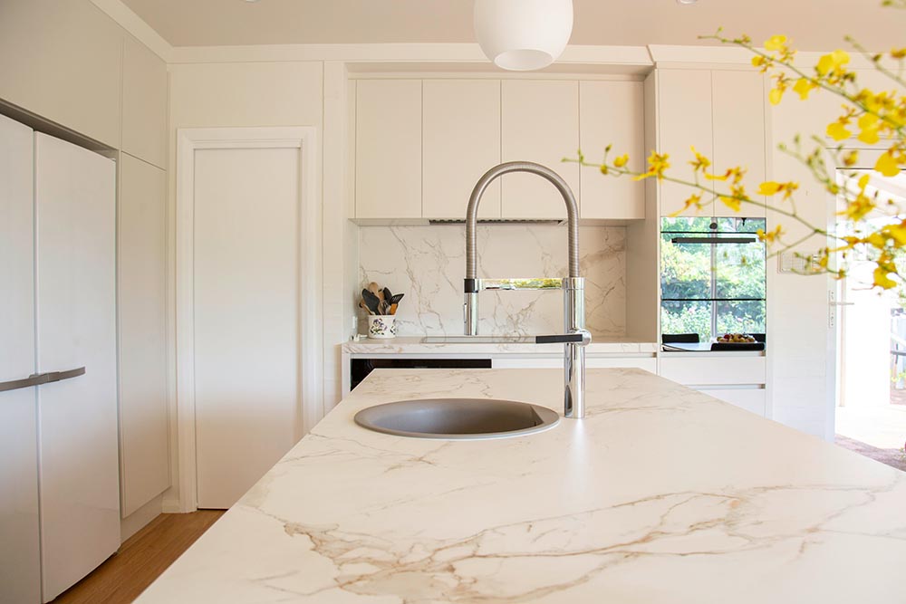 Kitchen remodel in New York with white marble countertops, a large island featuring a round sink and flexible chrome faucet, and light-colored cabinetry.