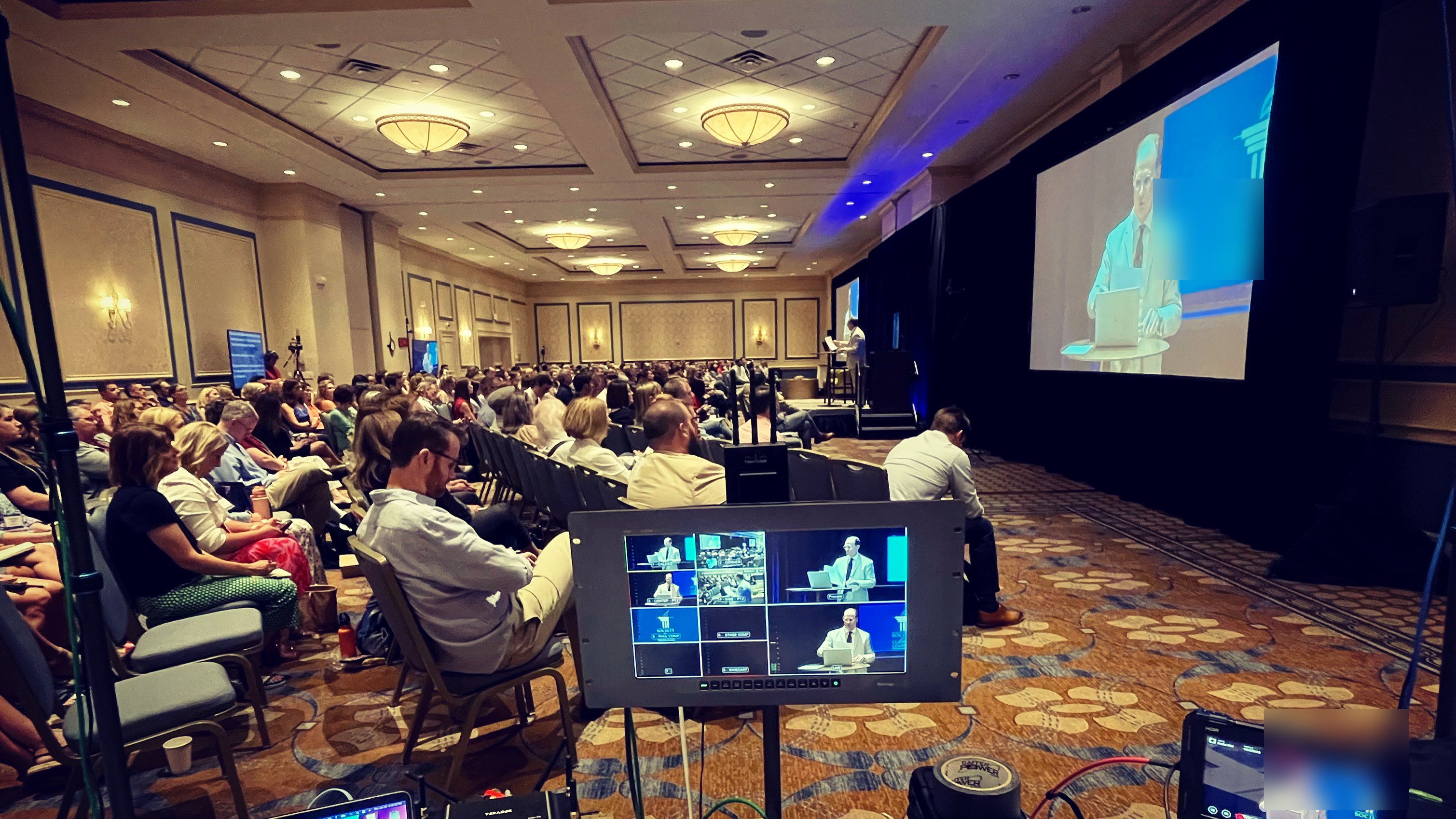 Ballroom corporate event webcast production: multiview monitor at the back of a full conference room with the speaker on the big screen