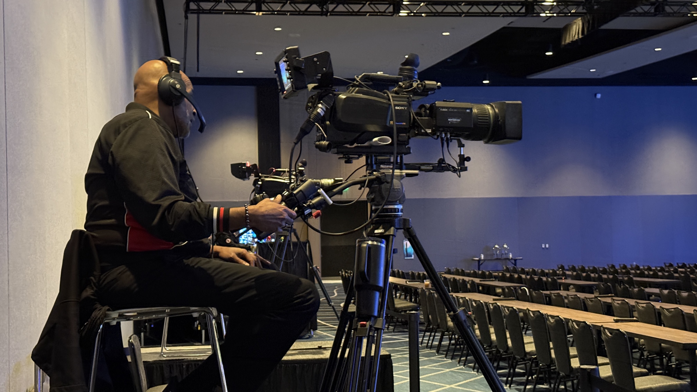 Corporate event videographer with a broadcast camera on a tripod in a hotel ballroom before a conference