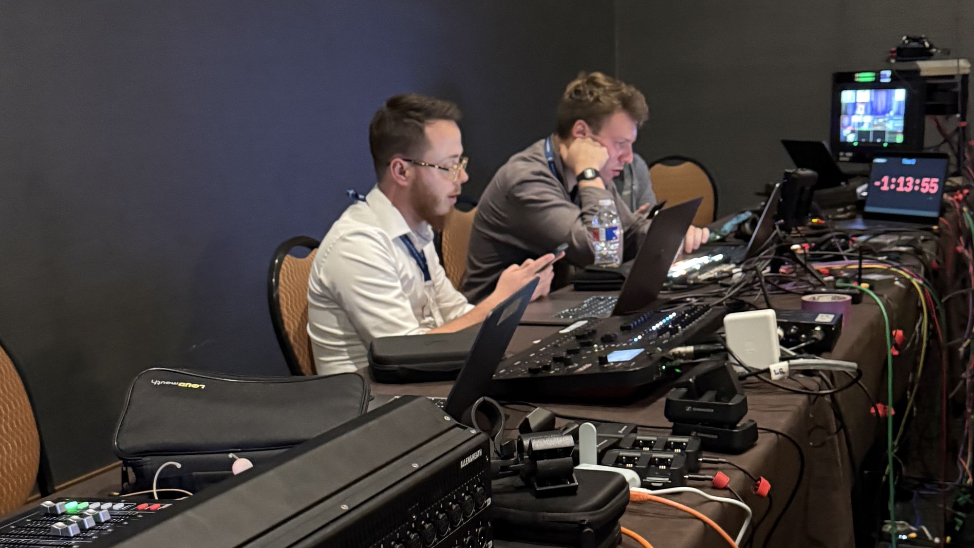 Two livestream crew members at a backstage production desk with an Allen & Heath SQ5 mixer, switcher, and show timer