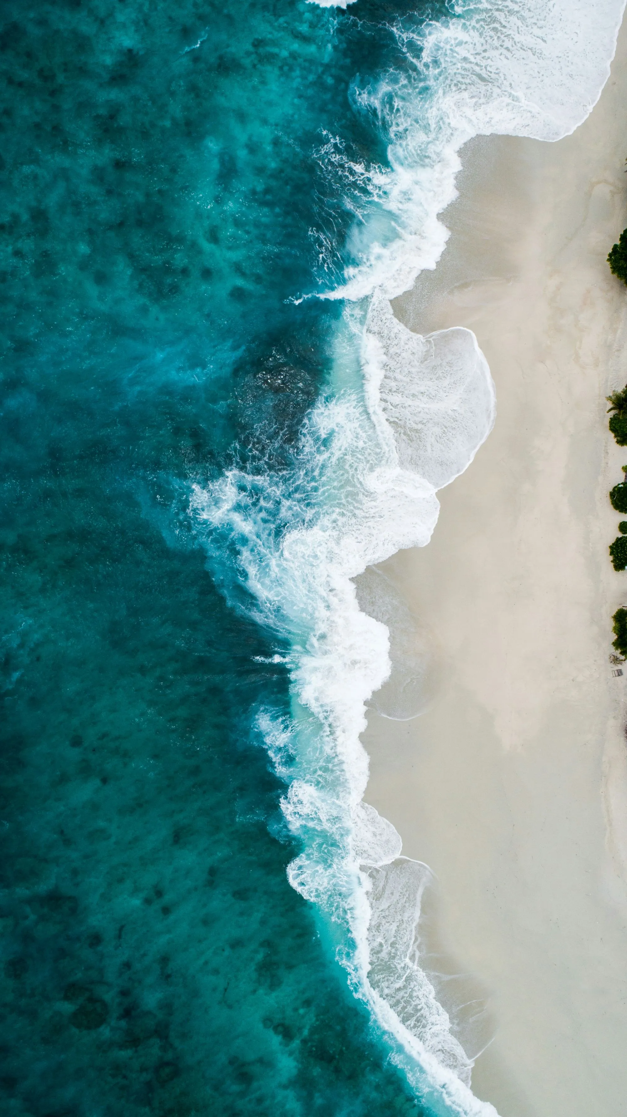 Draufsicht von einem Strand mit blauem Meer und Wellen.