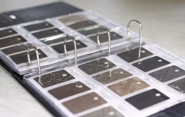 Binder displaying a collection of stone or laminate countertop samples in various shades of grey, brown and black, commonly used for interior design or kitchen renovation selections.