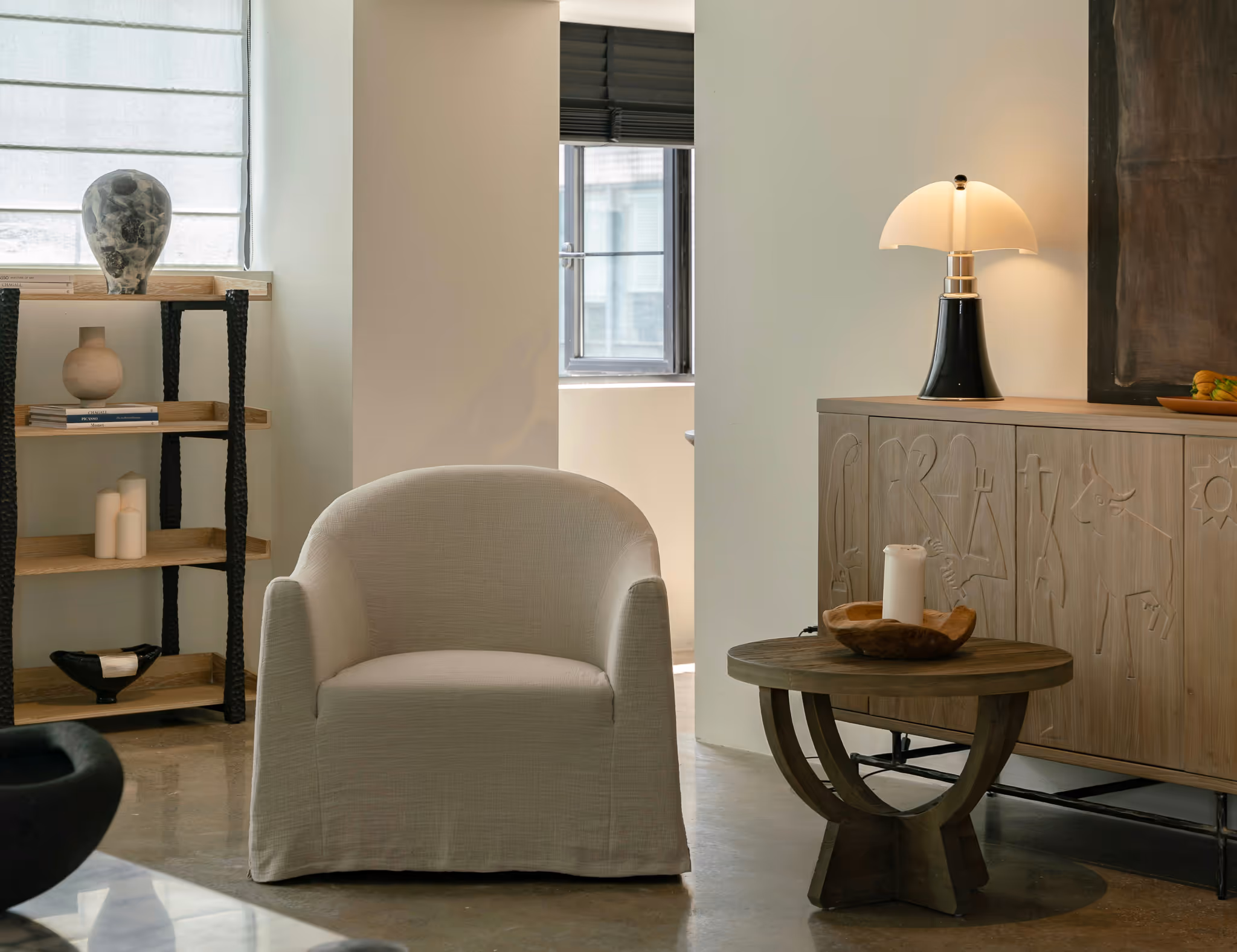 Scandinavian-style living room with beige armchair, round wooden side table, unique carved sideboard, and modern black lamp