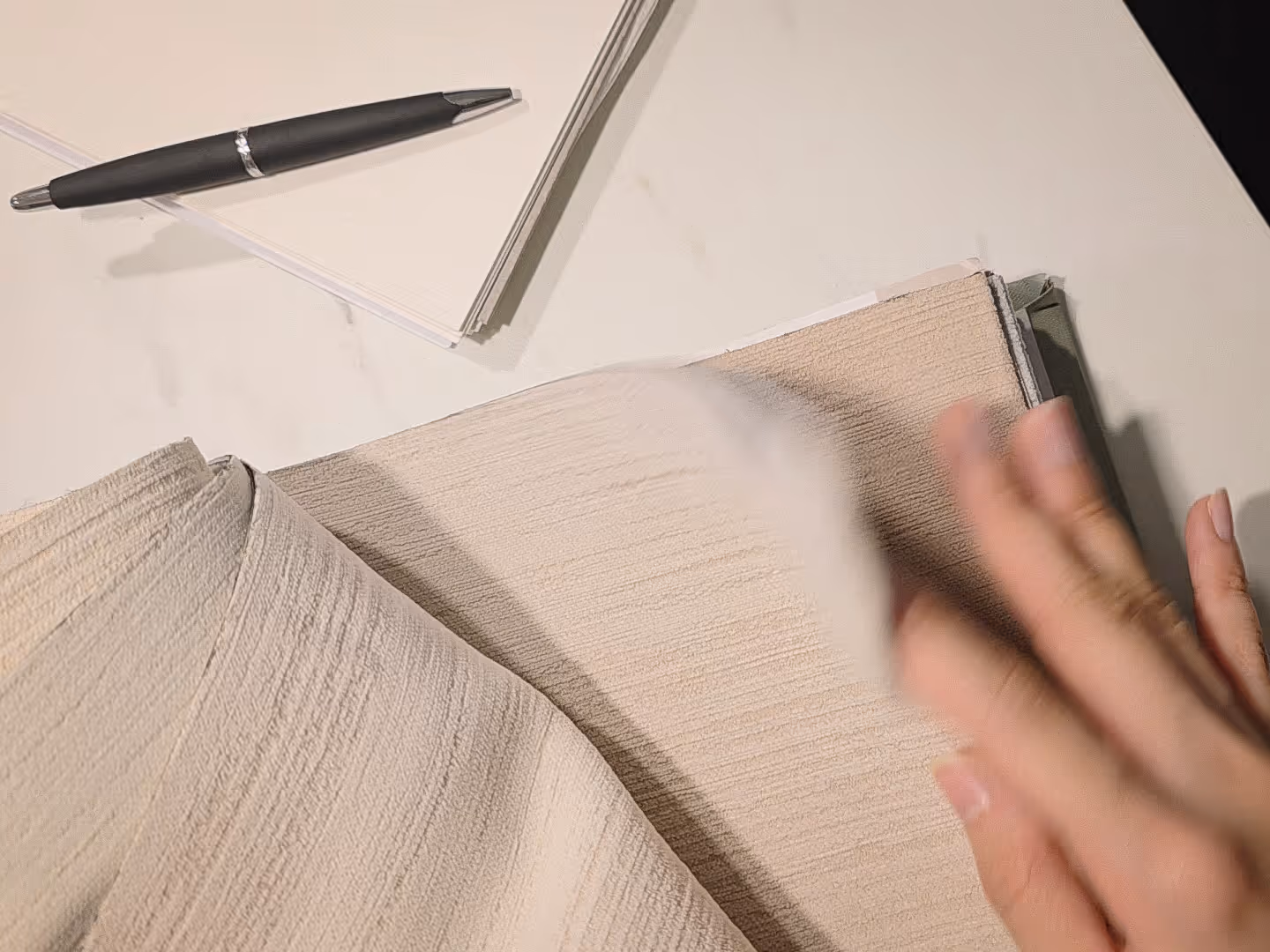 Close-up of beige curtain fabric samples in a swatch book, designer hand flipping through options