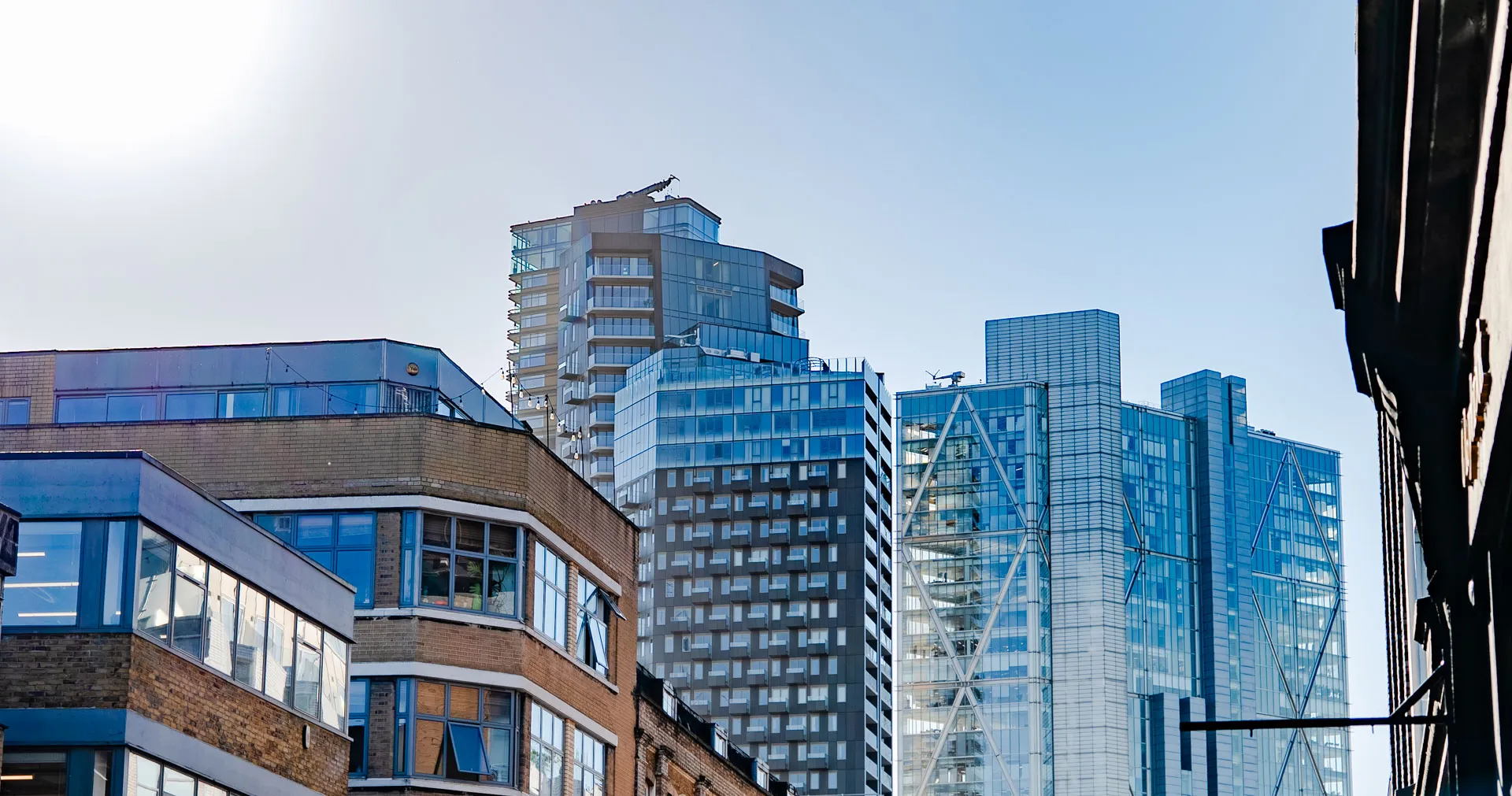 Modern glass skyscrapers and brick buildings under a clear blue sky with the sun shining brightly.