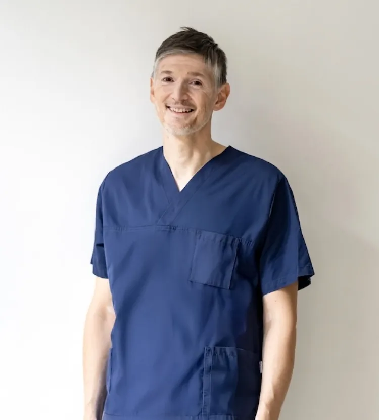 Porträt des sympatisch und vertrauensvoll lächelnden Dr. Vladan Montenegro in dunkelblauer medizinischer Schutzkleidung vor weißem Hintergrund.