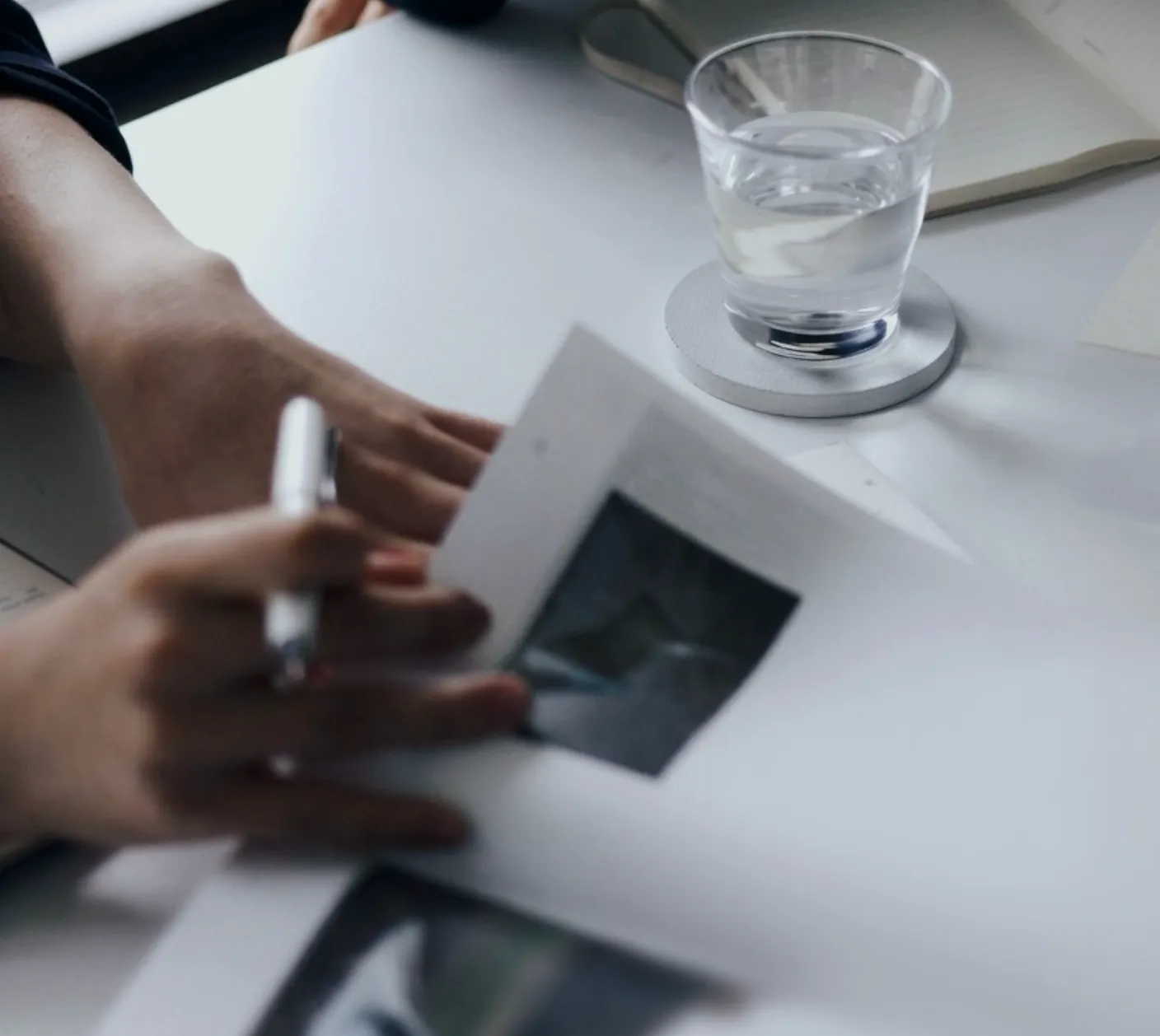 Person reviewing printed visual materials at a desk beside a notebook and a glass of water.
