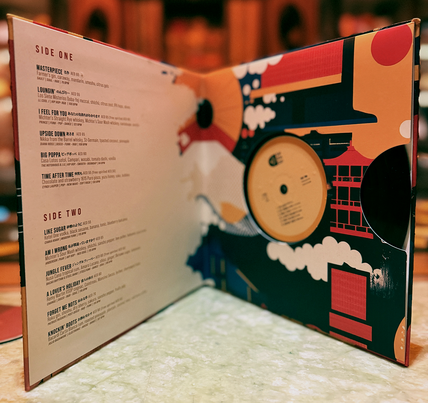 Open ten inch vinyl cocktail menu at Saikindo listening bar, showing track-inspired drink names and illustrated record sleeve artwork.