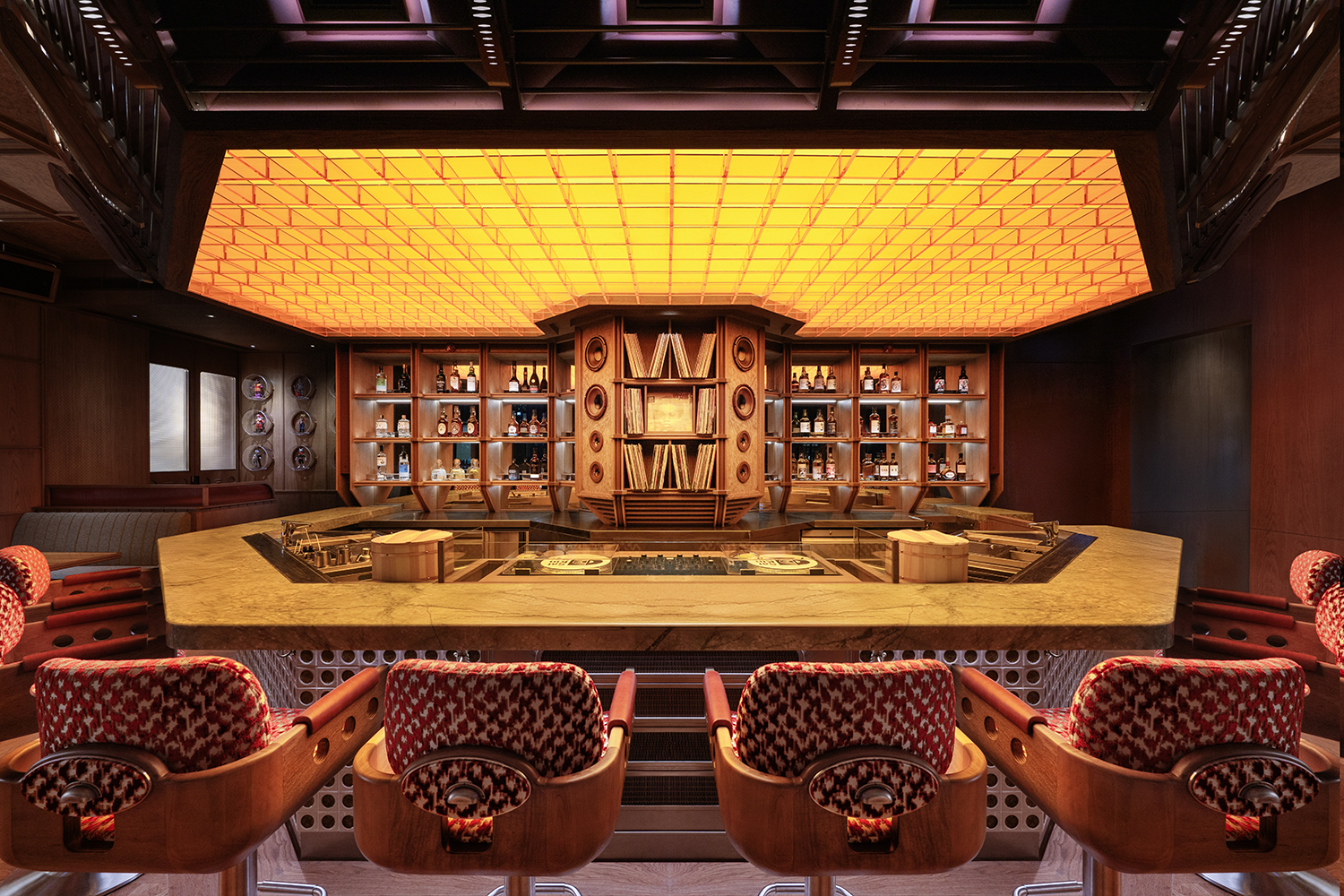 Central bar and DJ booth at Saikindo listening bar in Abu Dhabi, featuring integrated speakers, vinyl shelving, custom seating and warm acoustic lighting.