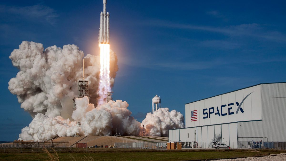 A SpaceX Falcon Heavy rocket lifting off from the launch pad in daylight.