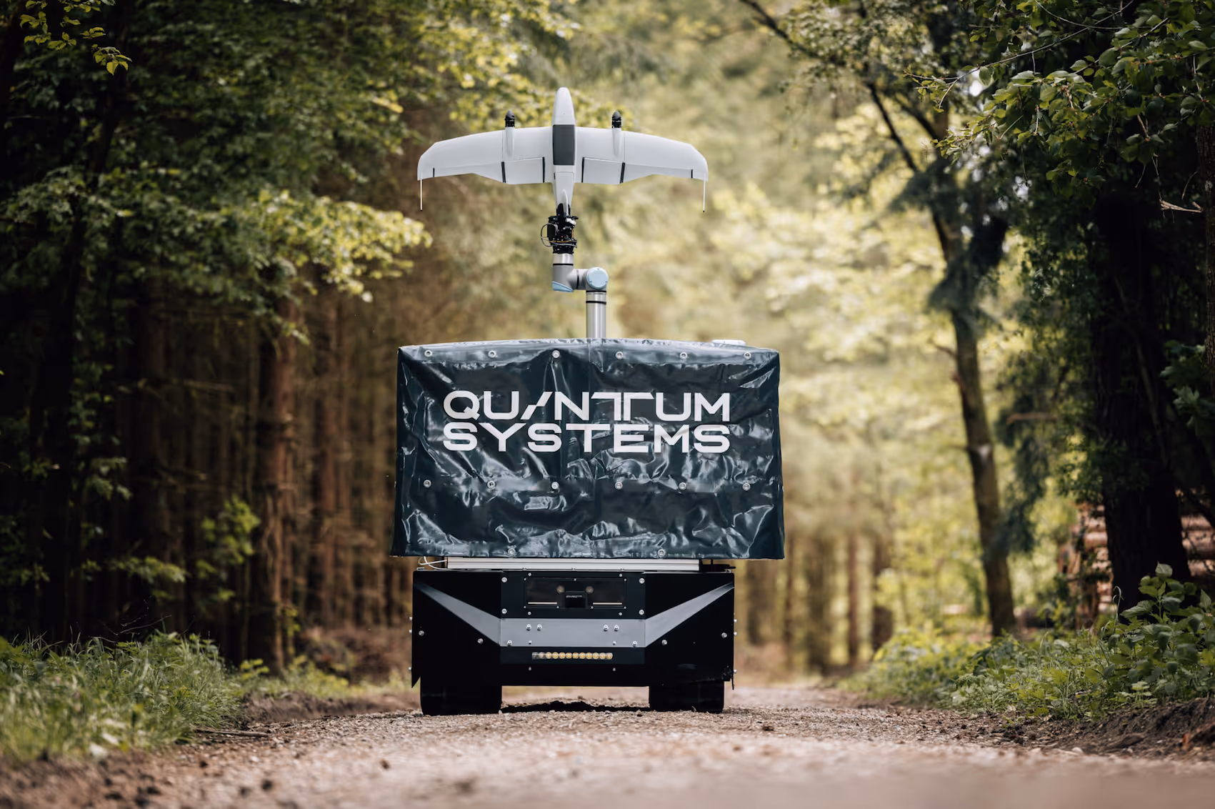 Autonomous vehicle with 'Quantum Systems' cover and drone mounted on top, on a forest path.