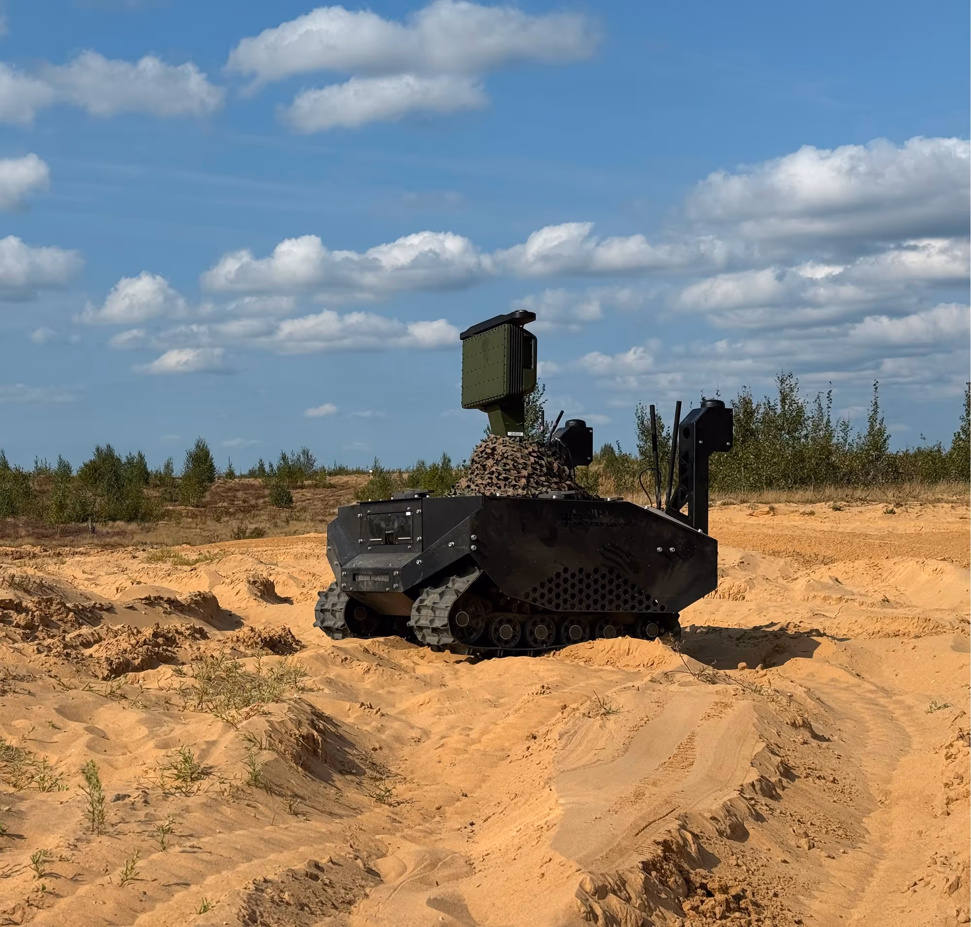 Tracked robotic vehicle equipped with sensors navigating sandy terrain under a partly cloudy sky.