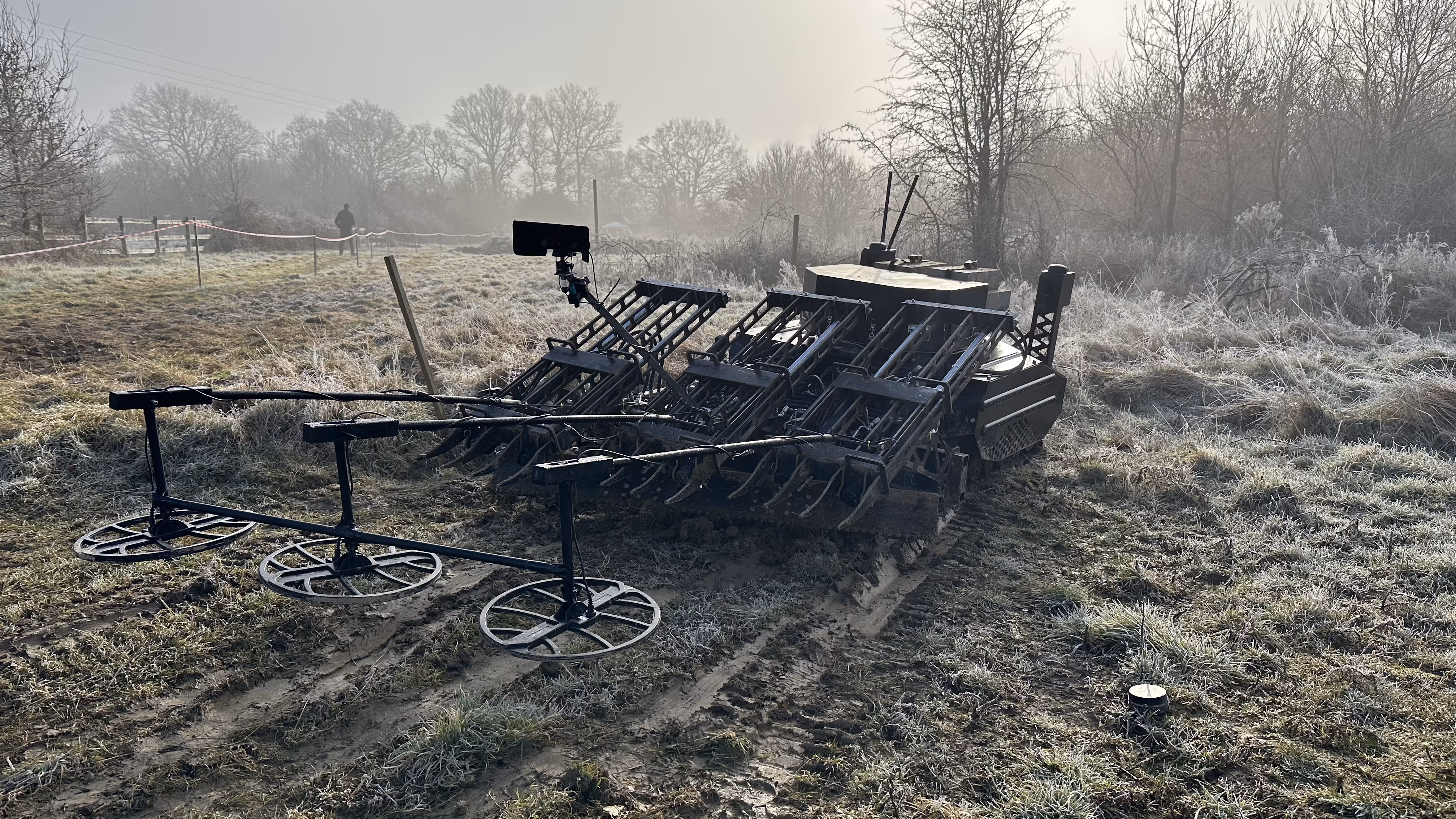 Robotic agricultural machine with three large metal discs and tines on frosty ground in a misty rural field.