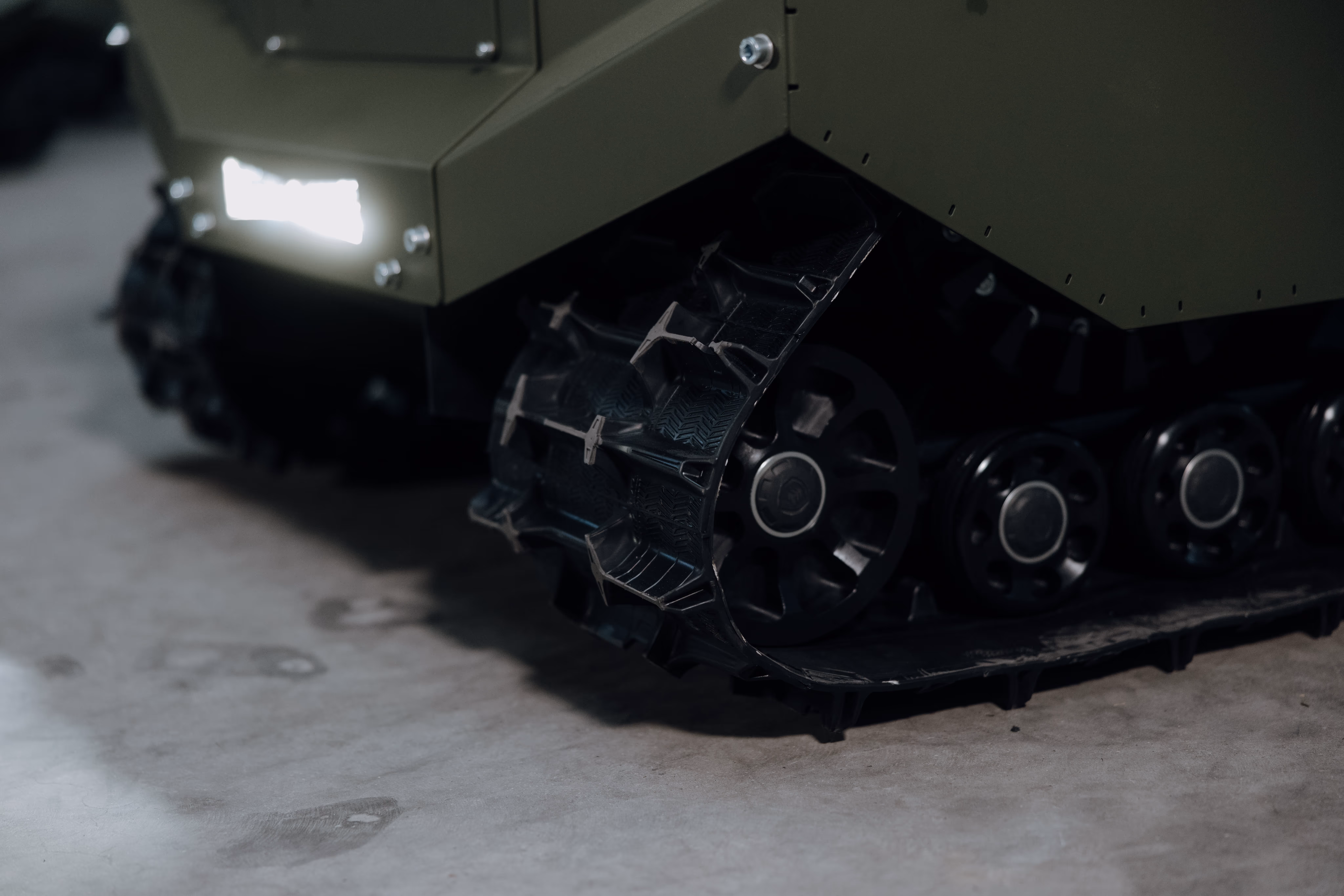Close-up of the black rubber track and wheels of a military-style robotic vehicle on a concrete floor.