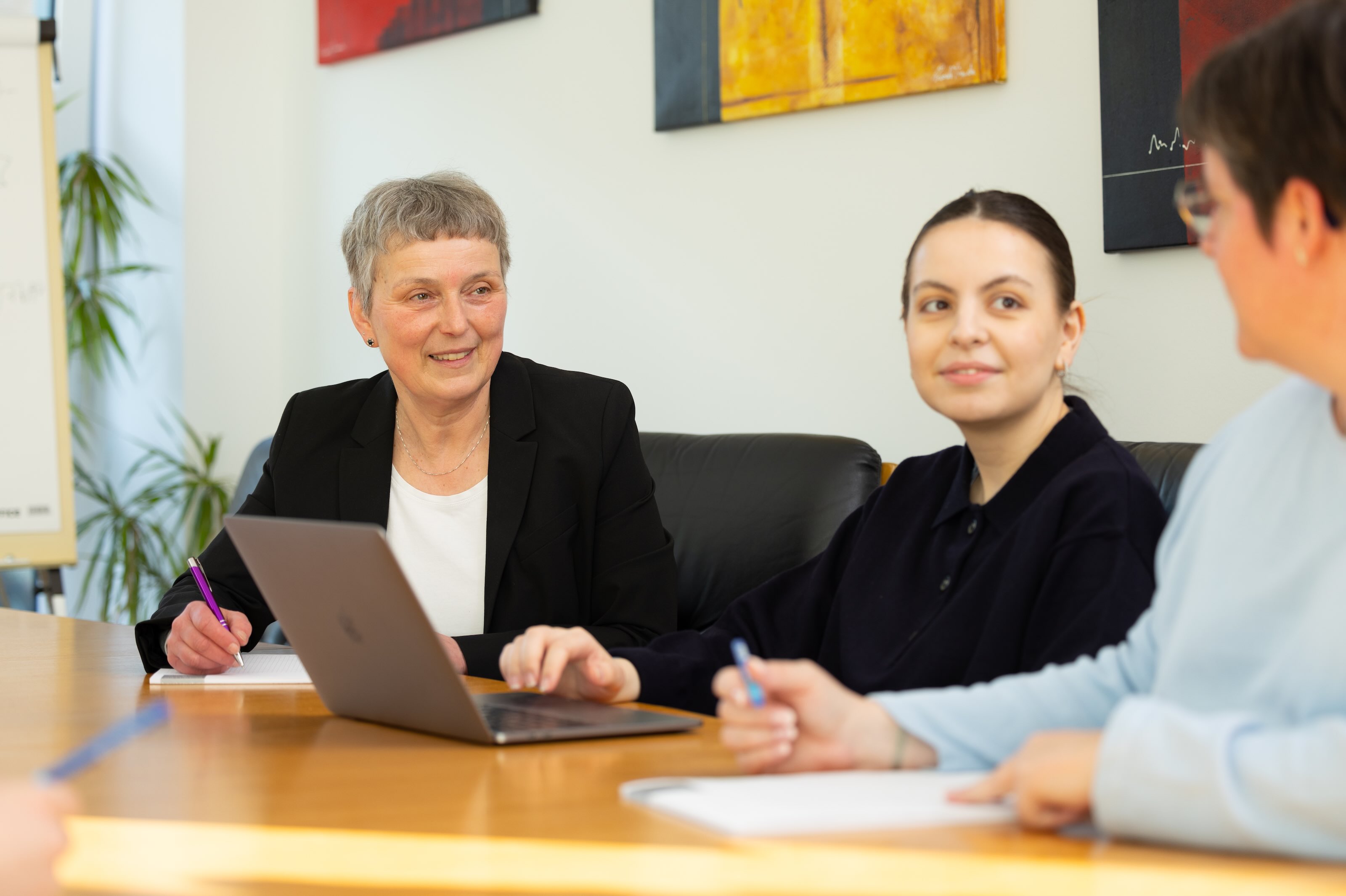 Drei Frauen im Gespräch am Tisch mit Unterlagen.
