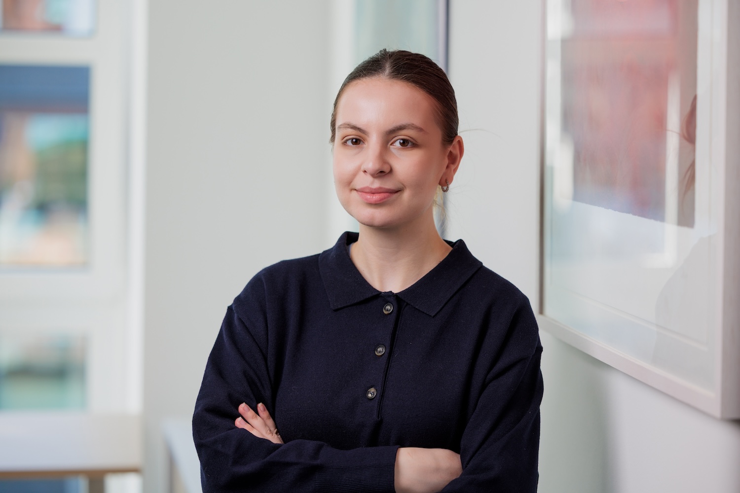 Porträt einer Frau mit dunklen Haaren im dunklen Oberteil, Arme verschränkt.