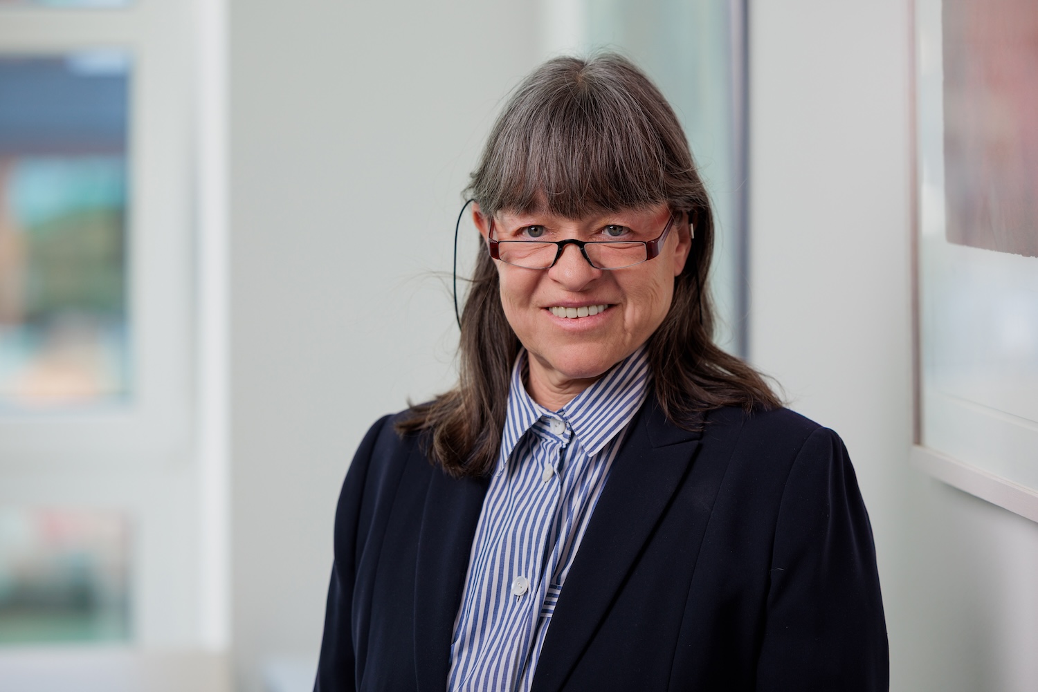 Porträt einer Frau mit Brille im dunklen Oberteil, lächelnd.
