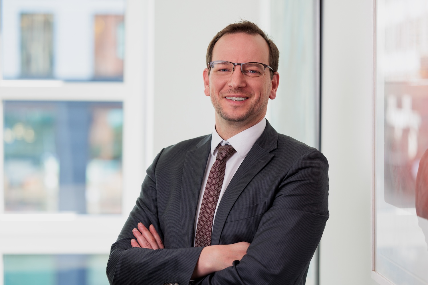 Porträt eines Mannes im Anzug mit Brille, Arme verschränkt.