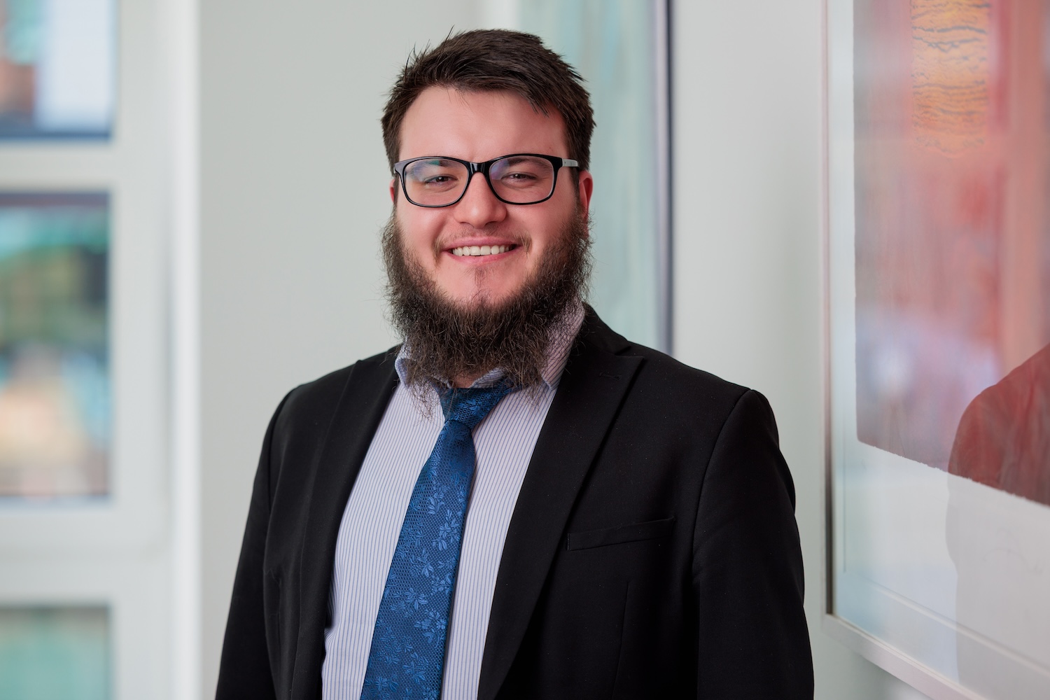 Porträt eines Mannes mit Brille und Bart im Anzug, lächelnd.