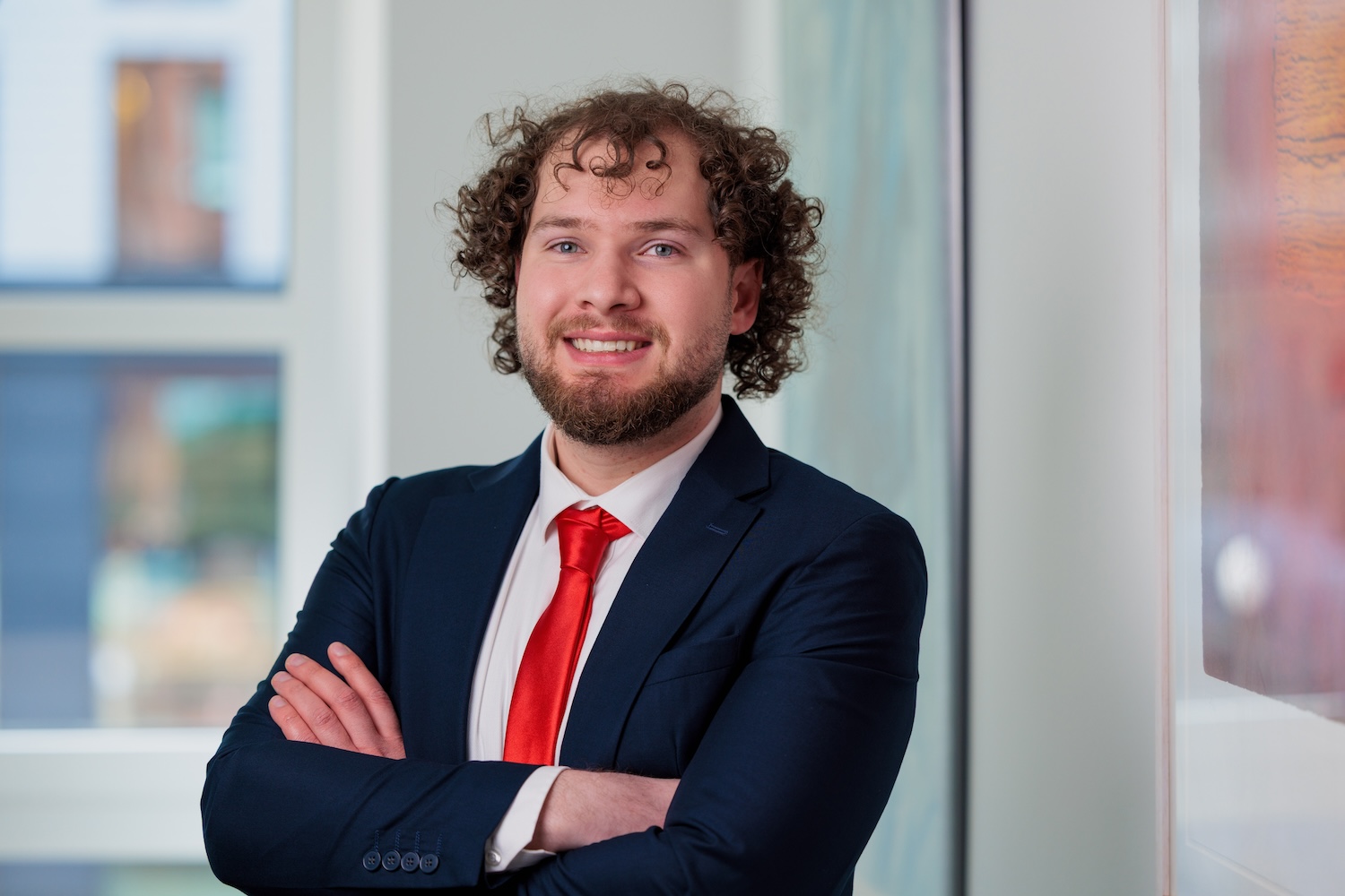 Porträt eines Mannes mit Bart und Locken im Anzug, Arme verschränkt.