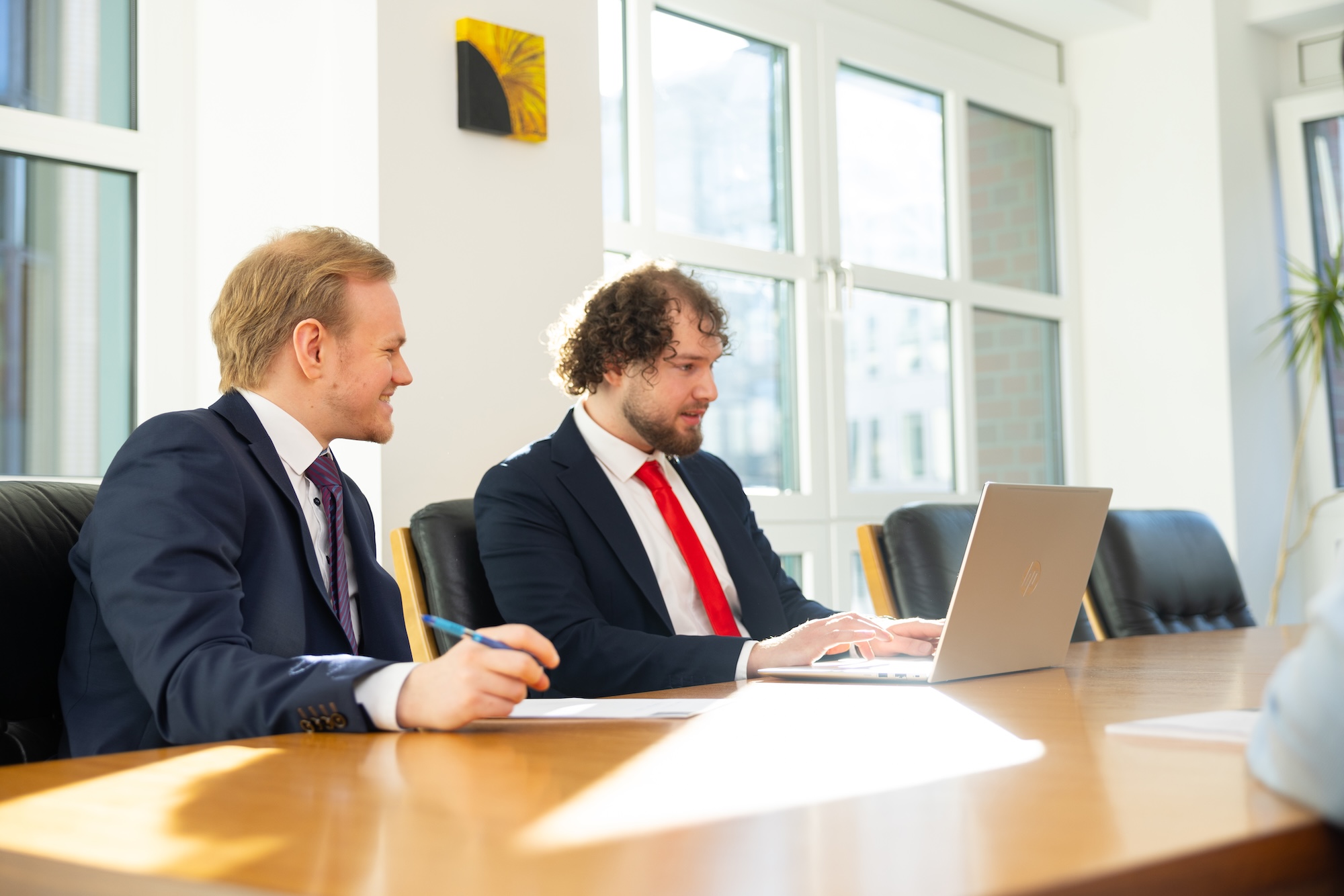 Zwei Männer im Anzug im Gespräch am Schreibtisch.