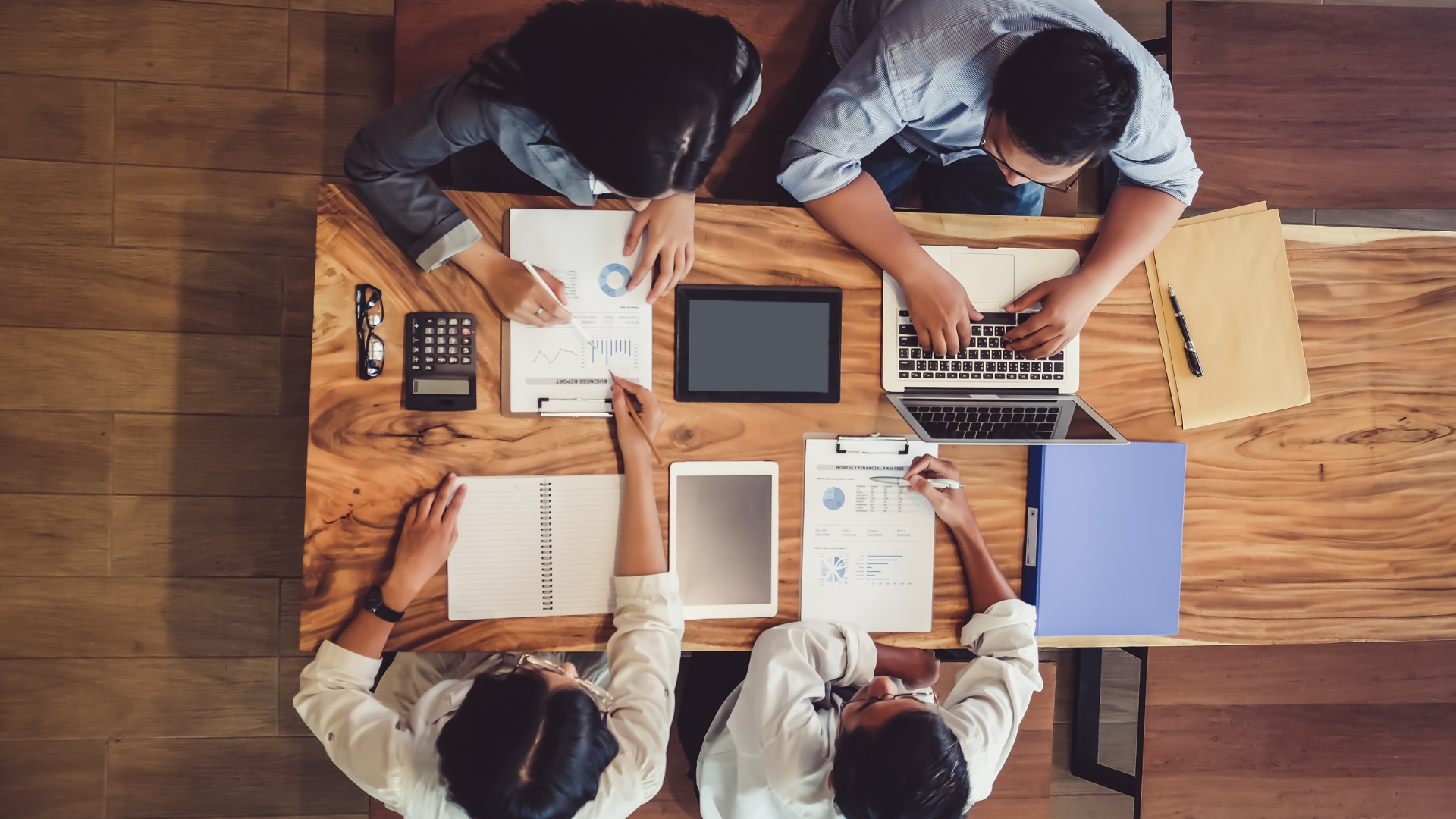 Teammeeting von oben, mehrere Personen am Tisch mit Unterlagen.