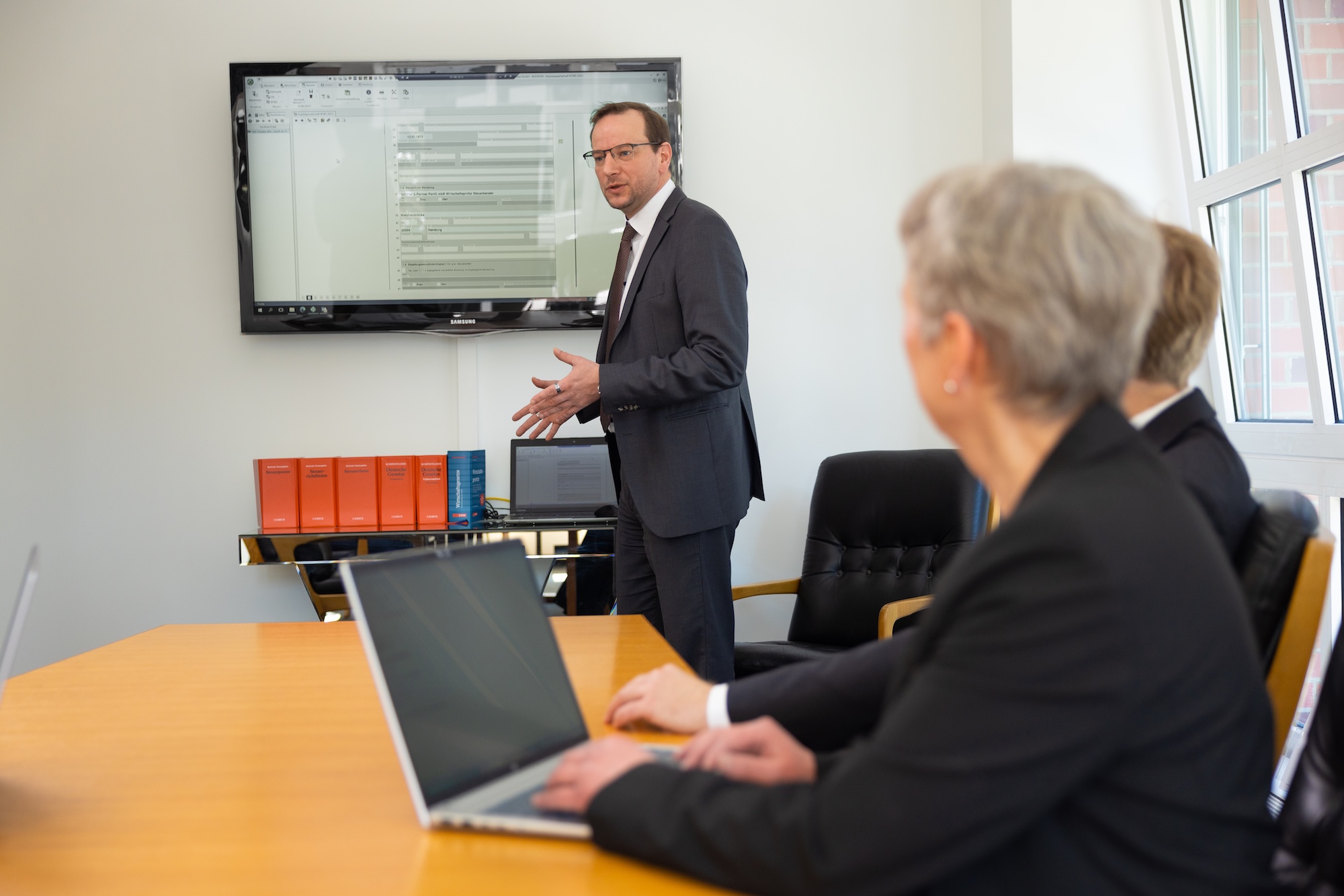 Person präsentiert am Bildschirm, andere Person hört zu und macht sich Notizen.