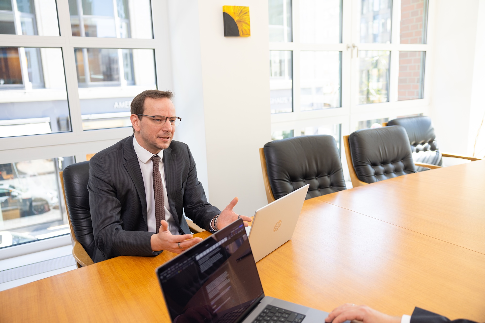 Mann im Anzug sitzt am Konferenztisch mit Laptop.