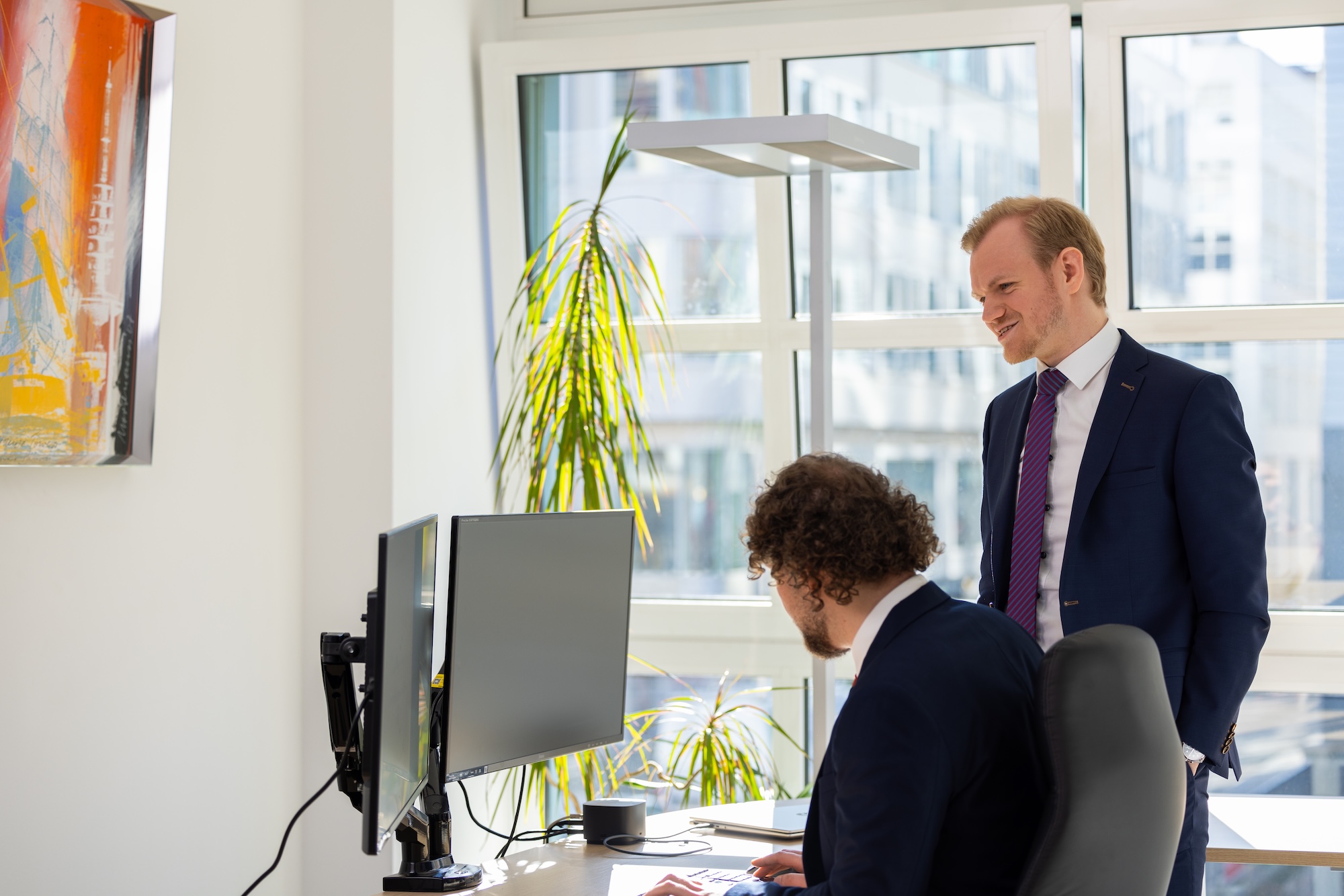 Zwei Männer im Gespräch, einer steht, einer sitzt am Schreibtisch.