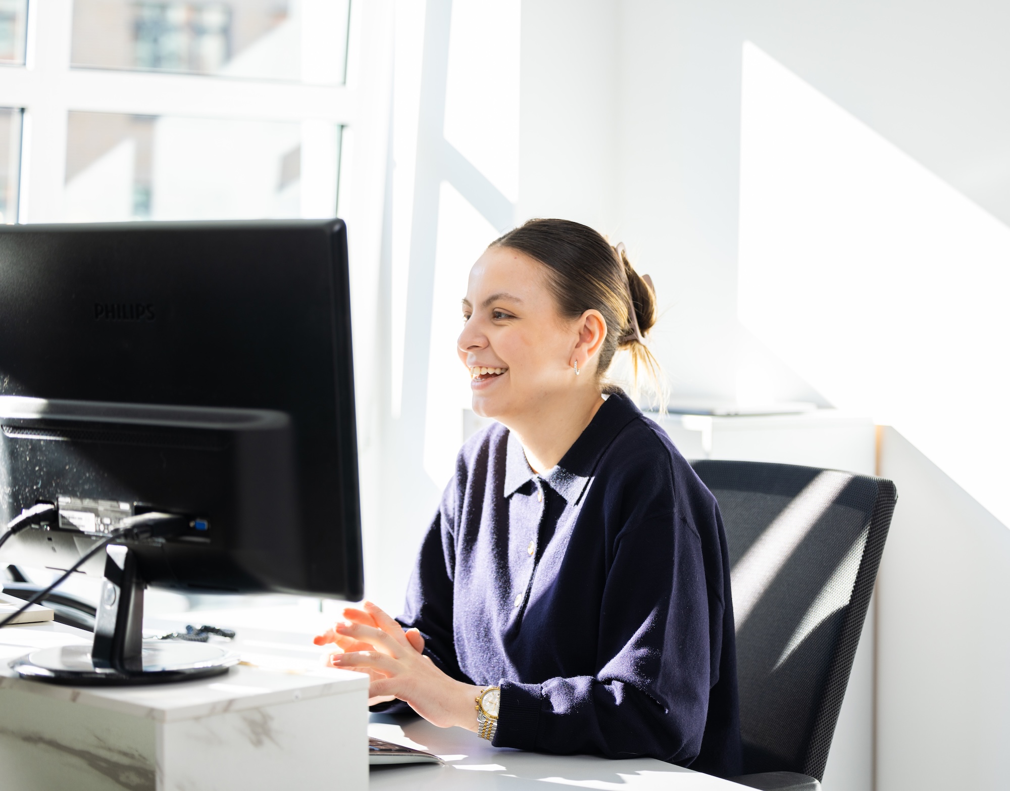 Frau am Schreibtisch tippt am Computer, trägt Business-Kleidung.