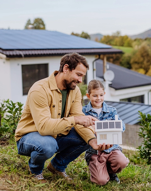 Kleines Mädchen zeigt ihrem Vater ein Papiermodell eines Hauses mit Solarmodulen und erklärt, wie es funktioniert. 