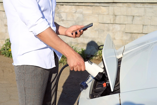 Ein Mann mit einem Telefon in der Hand verbindet ein Elektroauto mit dem Ladegerät.