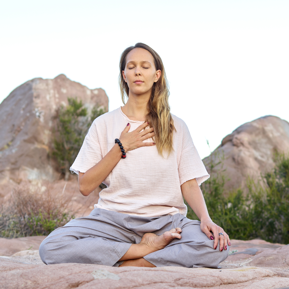 Woman seen in profile laying down on yoga mat in the grass with closed eyes looking serene