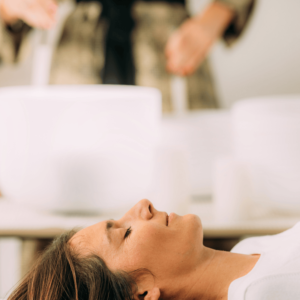 Woman seen in profile laying down on yoga mat in the grass with closed eyes looking serene