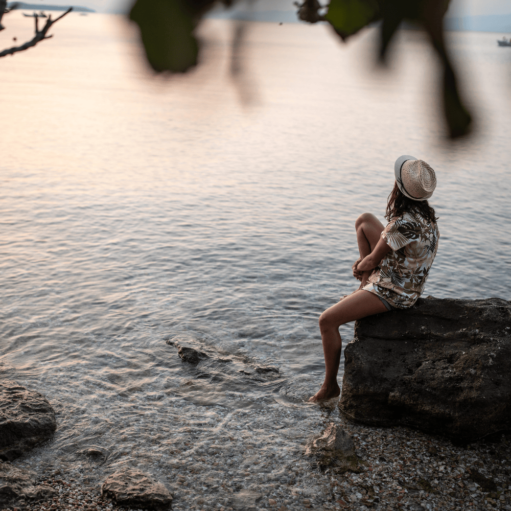 Woman seen in profile laying down on yoga mat in the grass with closed eyes looking serene