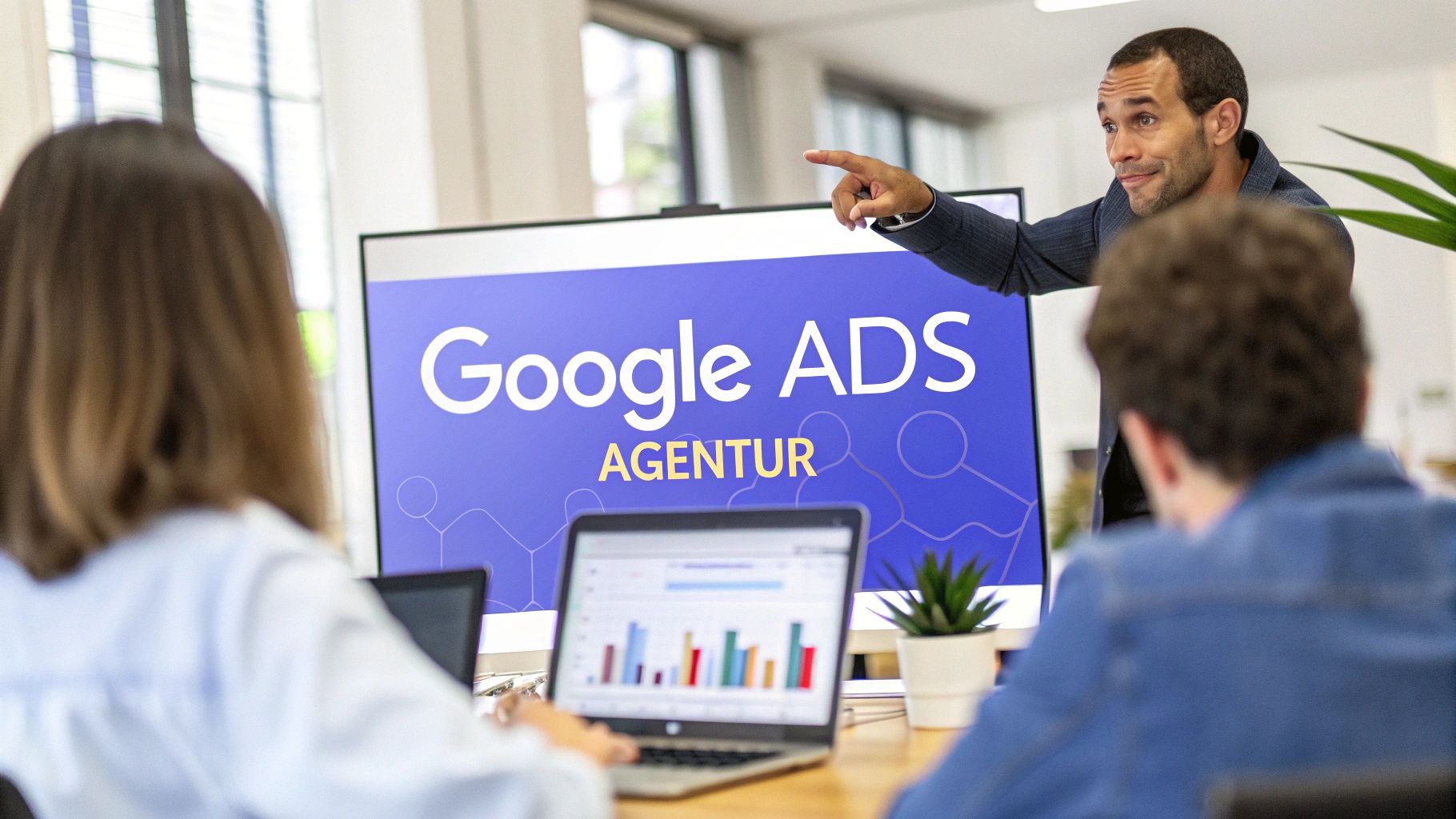 Auf einer Tafel steht "Google Ads Agentur". Nebendran steht ein Mann mit dem Finger in eine Richtung zeigend und im Vordergrund sitzen ein Mann und eine Frau mit dem Rücken ur Kamera auf die Tafel schauend.