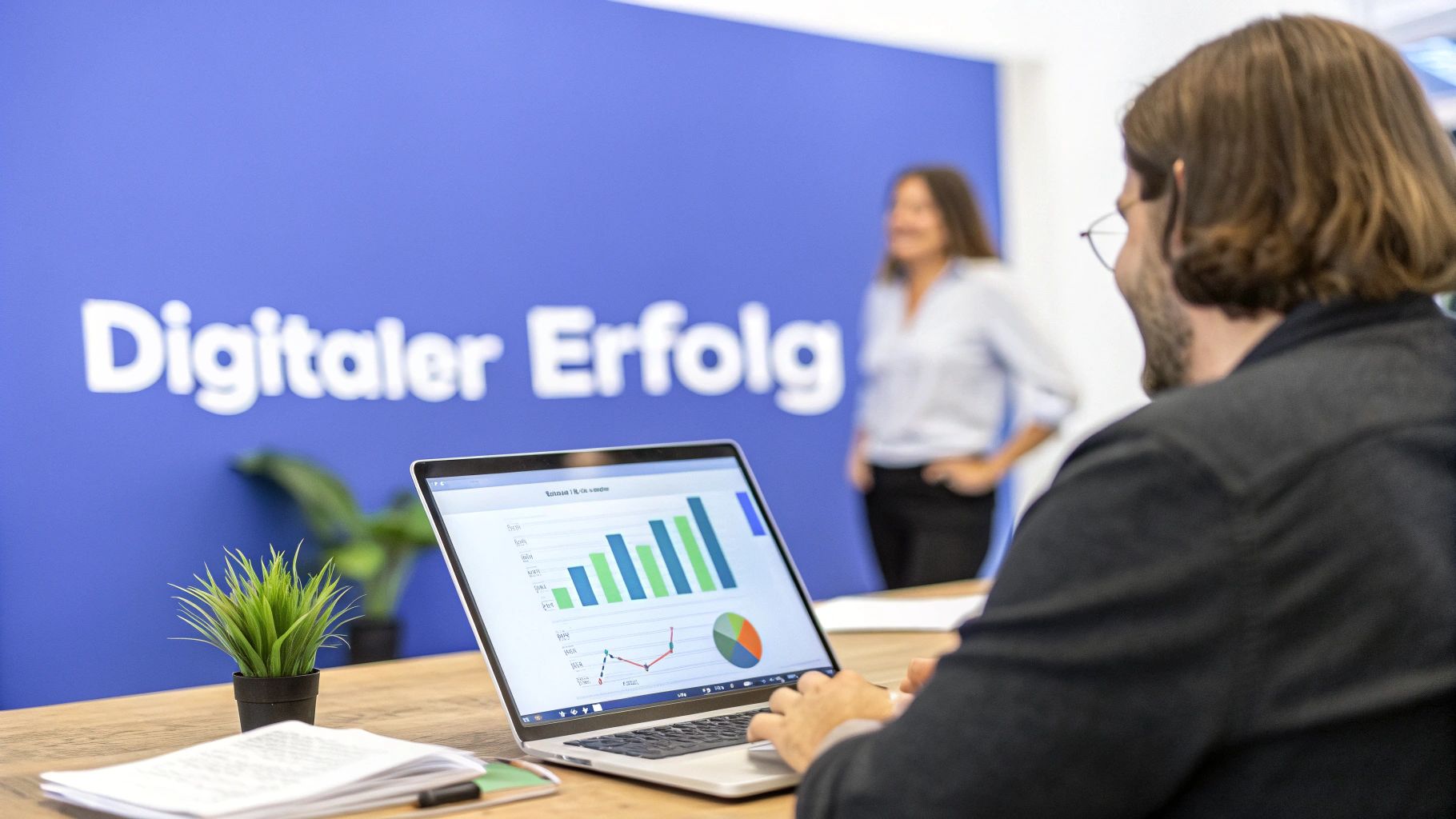 Mitarbeiter analysiert Daten auf einem Laptop vor einer Wand mit der Aufschrift 'Digitaler Erfolg' in einer SEO-Agentur.