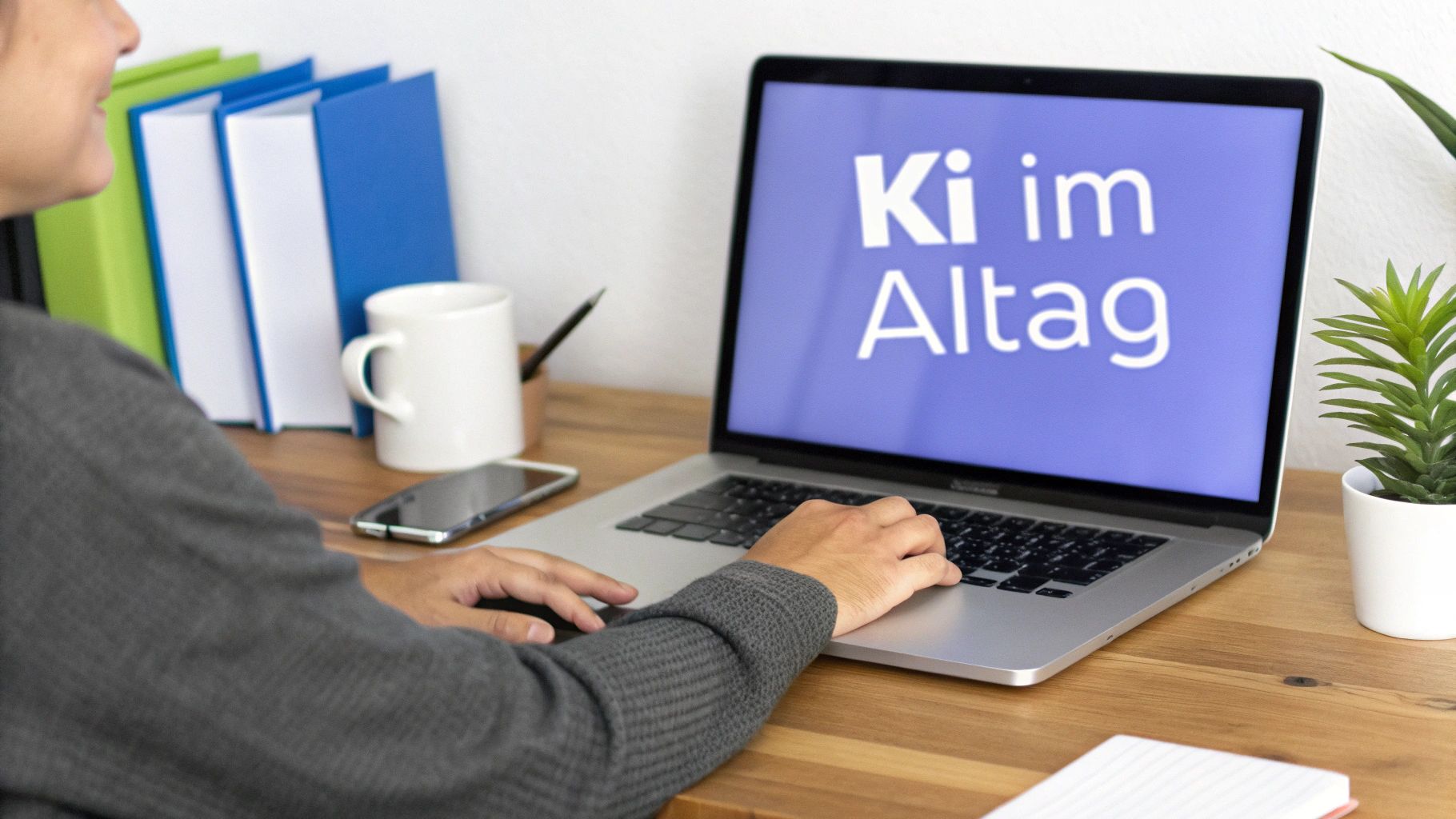 Eine Person arbeitet an einem Laptop mit der Aufschrift 'Ki im Alltag' auf dem Bildschirm. Ein Schreibtisch mit Ordnern, Tasse, Handy und Pflanze.