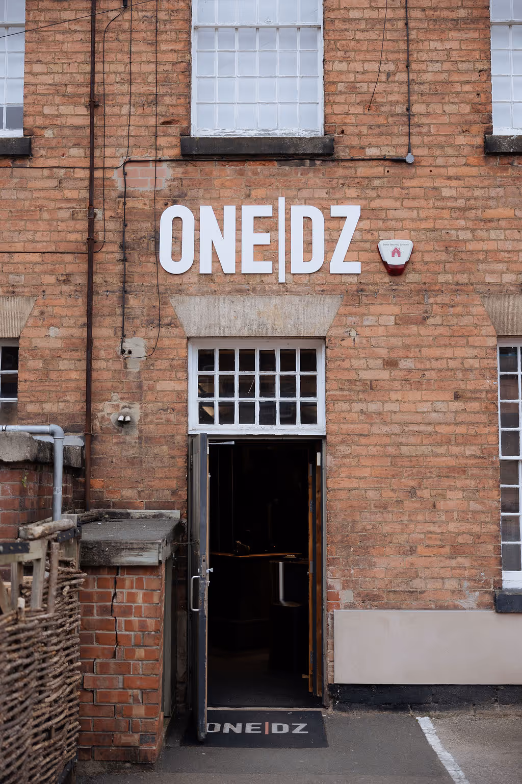 Entrance door to a brick building with white sign reading ONE|DZ and a matching doormat.