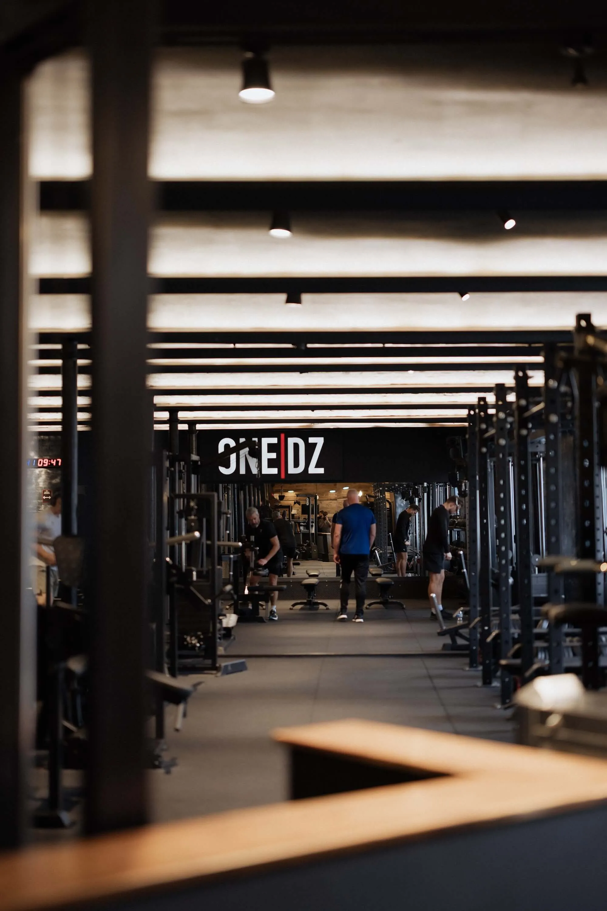 View of the ONE|DZ Gym Derby floor with members training, modern strength equipment, and free weights.