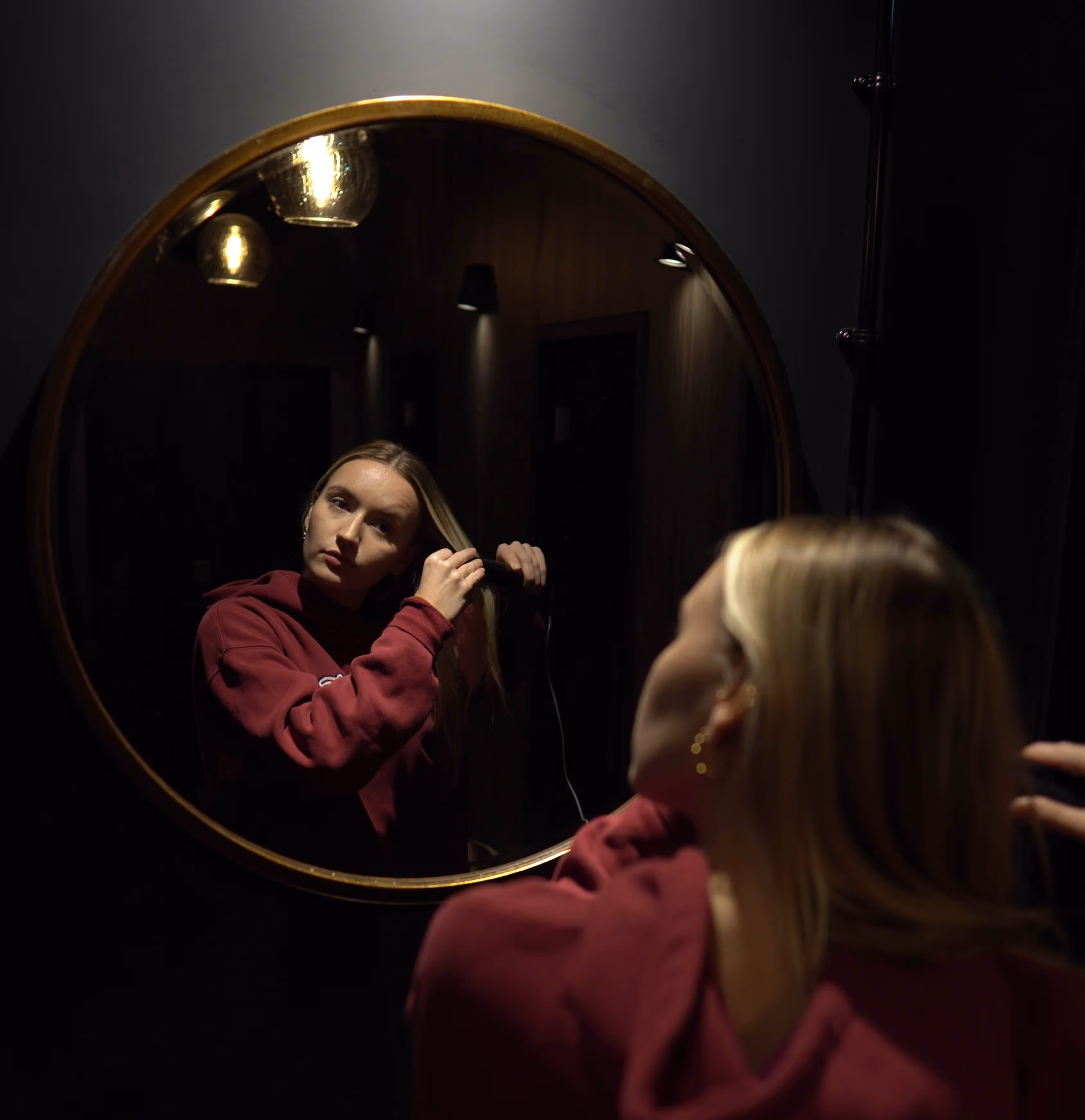 Woman straightening hair in front of a round mirror inside the infrared sauna room at ONE DZ Gym in Derby